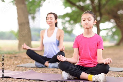Mother and daughter doing yoga exercises on grass in the park