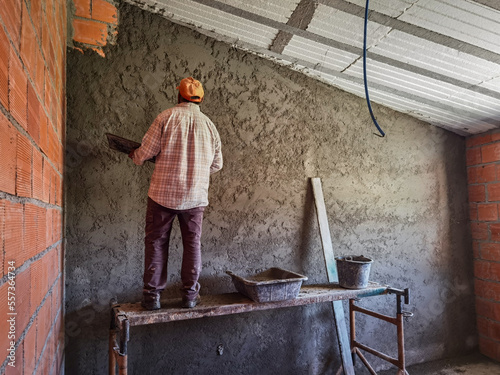 Trabalhador pedreiro a colocar cimento no muro para finalizar a parede com o reboco