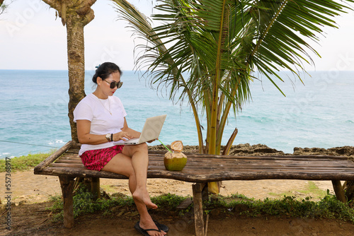 Smart young businesswoman teaching freelancer doing outdoor work on high seas background. working with a computer next to a coconut on the beach