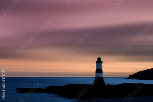 Lighthouse at sunrise with pastel coloured sky and sea creating silhouette shape of lighthouse