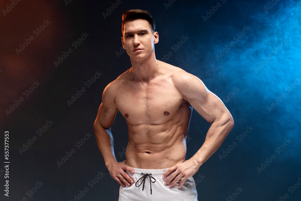 Athlete man with beautiful torso isolated on black background with coloured fume