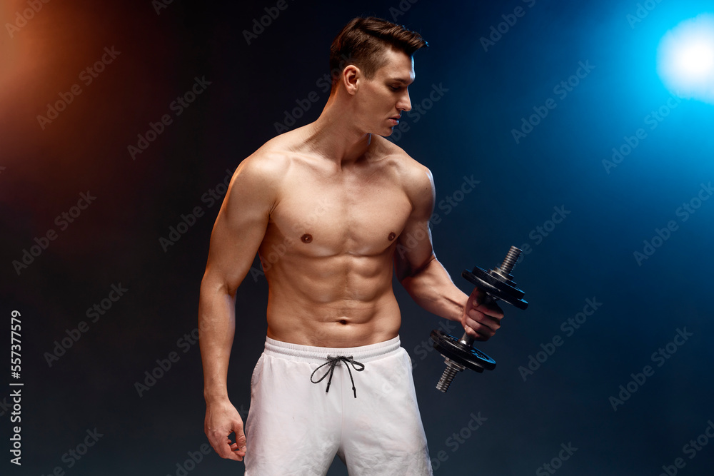Portrait of masculine young man holding dumbbell isolated on black background