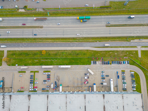 Aerial view of a logistics park with warehouse, loading hub and many semi trucks with cargo trailers standing at the ramps for load/unload goods at sunset.