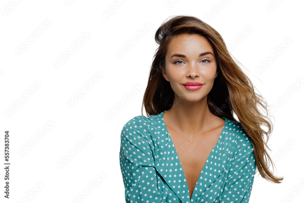 Studio shot of positive young woman has long wavy hair, makeup, wears turquoise polkadot blouse, looks straightly at camera, models against white background, copy space for your advertisement Studio shot of positive young woman has long wavy hair, makeup, wears turquoise polkadot blouse, looks straightly at camera, models against white background, copy space for your advertisement