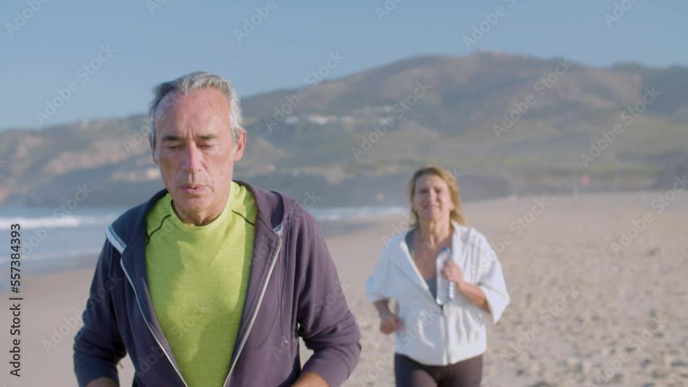 Focused man and woman running along ocean coast on summer day. Front view of mature couple in sportswear having intense cardio workout, doing physical activity in morning. Love, sport concept