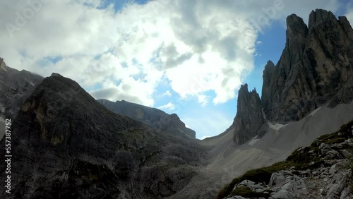 Rear view of woman with backpack and helmet hiking along a narrow pathway in Italian Dolomites, South Tyrol (Alto Adige), Italy, Europe. Massive mountains with very steep sharp slopes. Raw landscape