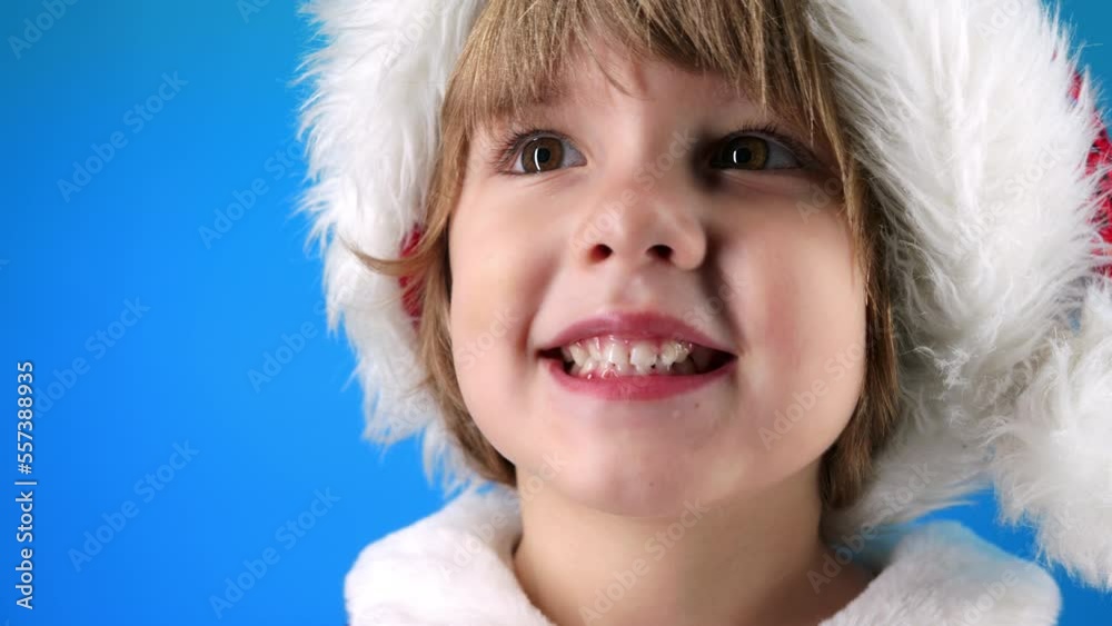 Portrait of adorable boy in Santa Claus hat on blue studio background. Christmas celebration. Happy childhood, kid, lovely son Portrait of adorable boy in Santa Claus hat on blue studio background. Christmas celebration. Happy childhood, kid, lovely son