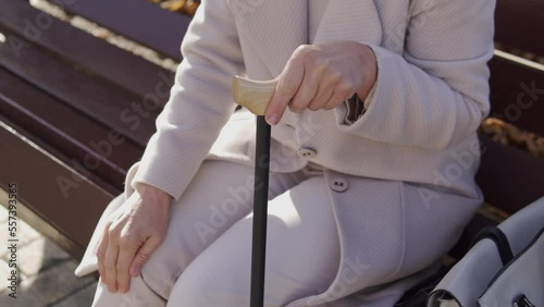 Mature woman with walking cane sitting on bench and rubbing sore knee, resting