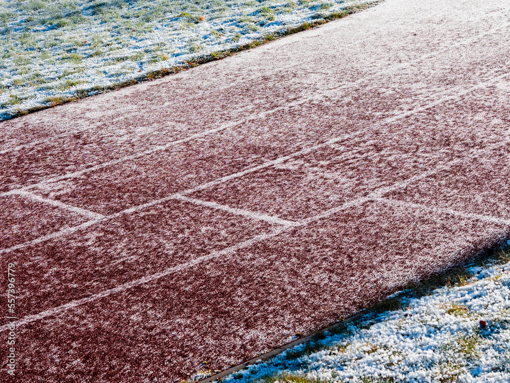 Fototapeta premium Running track partially covered with ice and snow. Dangerous surface conditions in winter cold season. Nobody. Sport training area.