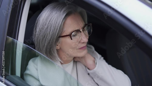 Senior businesswoman rubbing sore neck sitting in car, feeling numbness and pain