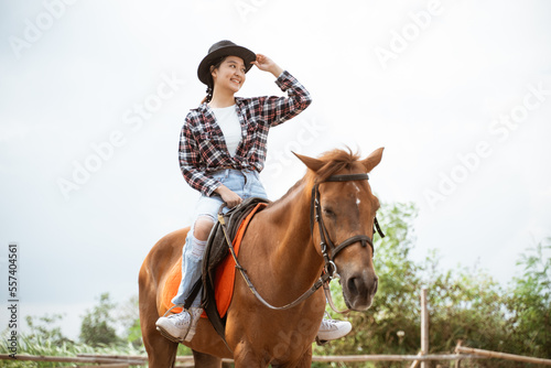 beautiful woman holding her cowboy hat while sitting on a horse at the ranch