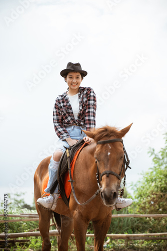 beautiful woman in cowboy hat smiling while sitting on horse at ranch