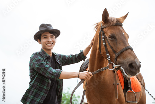 man in cowboy hat smiling while holding horse's head leash at the ranch © Odua Images