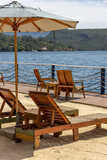 Empty wooden lounge chairs on the sand under green umbrella. In the background, a huge lake. Vertical
