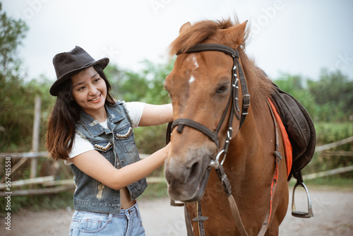 beautiful asian cowboy girl standing beside horse on outdoor background