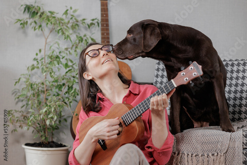 woman musician plays ukulele with abrador dog, sings. female music teacher leads online lesson or is resting photo