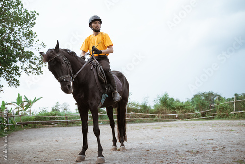 Male equestrian athlete wearing horse riding gear holding reins in court © Odua Images