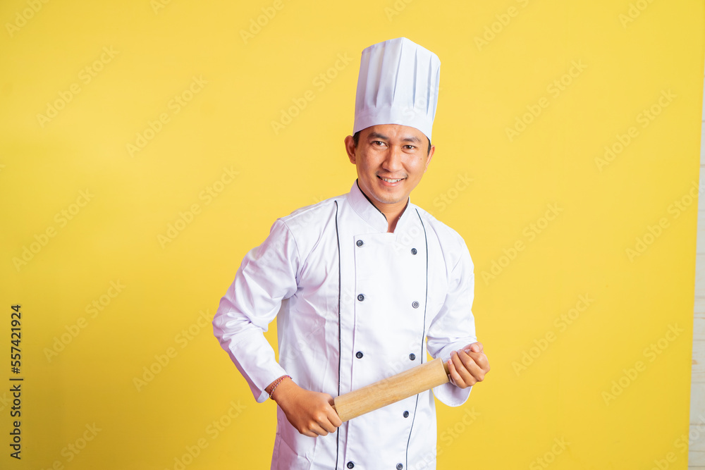 Asian chef smiling at camera while holding wooden rolling pin on isolated background Asian chef smiling at camera while holding wooden rolling pin on isolated background