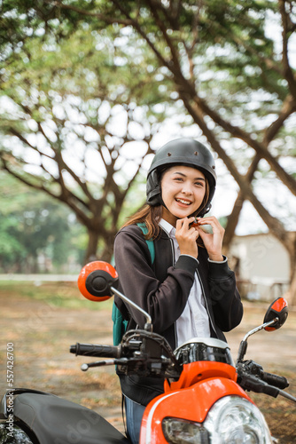 Attractive student girl wearing helmet strap while riding motorbike to school