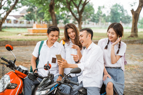 Four high school students selfie using smartphones together celebrating graduation on motorbike