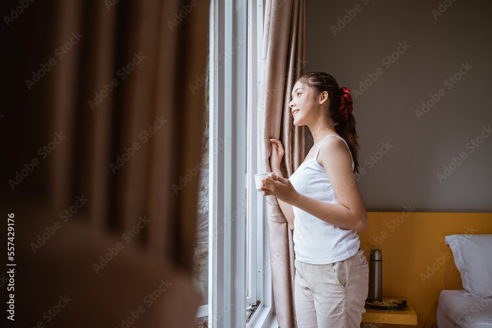 side view of smiling girl opening window curtains in the morning in bedroom side view of smiling girl opening window curtains in the morning in bedroom