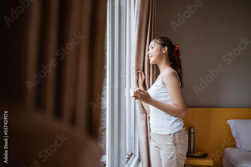 side view of smiling girl opening window curtains in the morning in bedroom