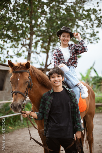 smiling cowboy girl riding horse and man holding reins on outdoor background © Odua Images