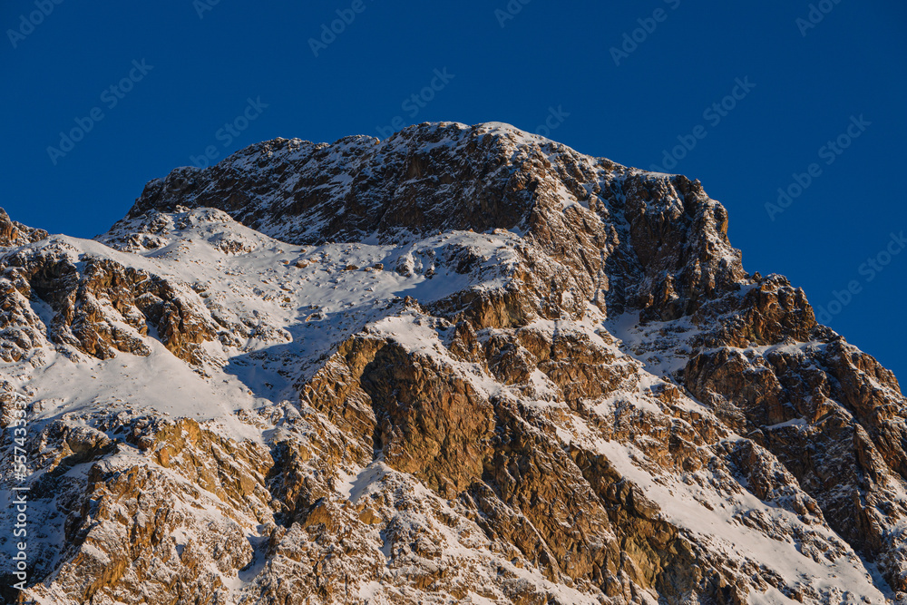 The first light of the sun illuminates the snowy mountains of the engadine, near the lake of Sils and the village of Sils, Switzerland - December 2022.