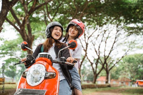 Two high school student girls wearing helmets and jackets enjoying a motorcycle ride together