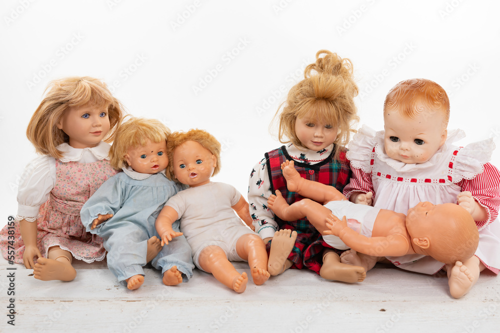 Collection of multiple dolls sitting on a rough white wooden table isolated on white with copy space Collection of multiple dolls sitting on a rough white wooden table isolated on white with copy space