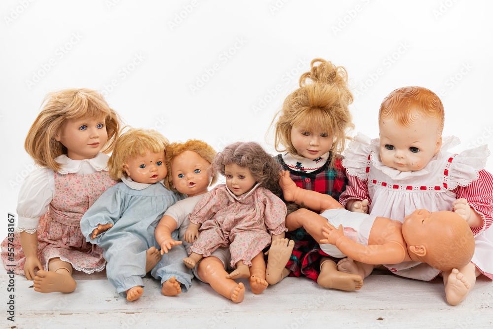 Collection of multiple dolls sitting on a rough white wooden table isolated on white with copy space Collection of multiple dolls sitting on a rough white wooden table isolated on white with copy space