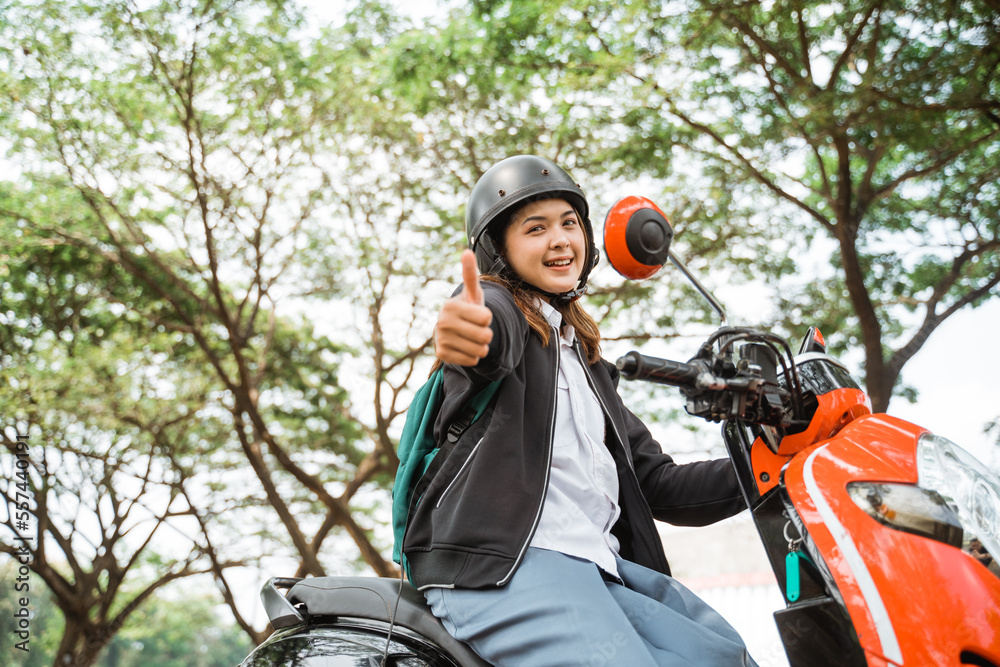 Asian student girl wearing helmet with thumbs up while riding motorbike to school Asian student girl wearing helmet with thumbs up while riding motorbike to school