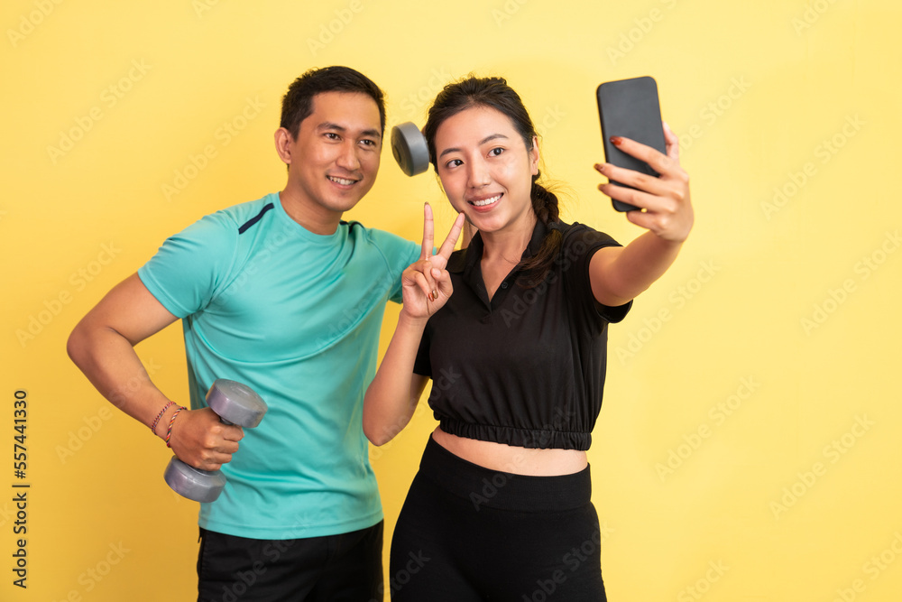 selfie woman using cellphone with man behind carrying dumbbell on isolated background selfie woman using cellphone with man behind carrying dumbbell on isolated background