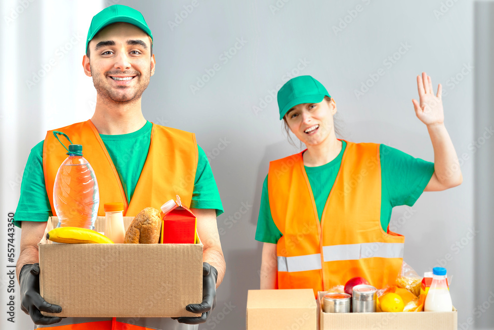 Help Collection Center, free food distribution. Volunteers wearing uniform green caps, t-shirts, orange vests prepare a food package grocery set for in-need people, sort, collect food donation boxes Help Collection Center, free food distribution. Volunteers wearing uniform green caps, t-shirts, orange vests prepare a food package grocery set for in-need people, sort, collect food donation boxes