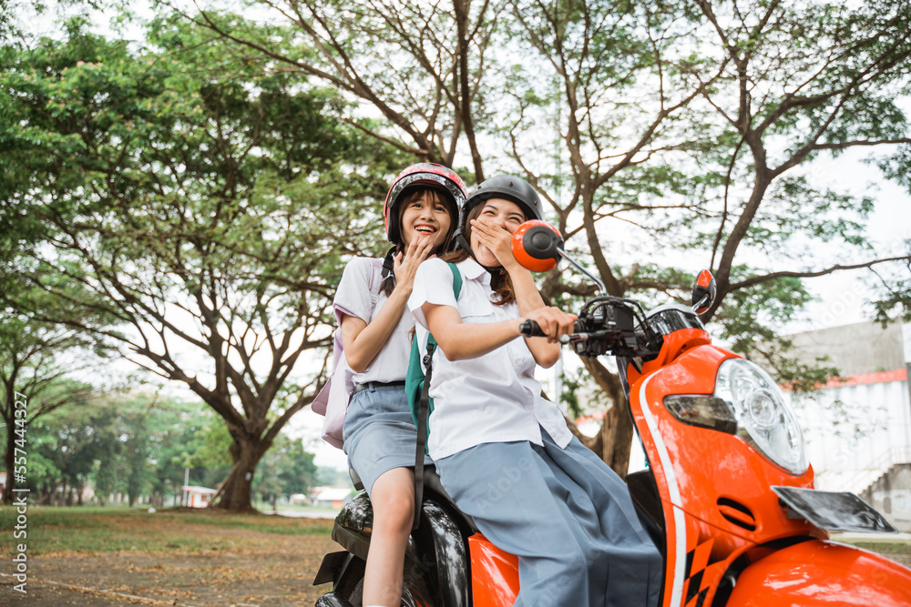 Two student girls wearing helmets laughing happily while riding a motorcycle together
