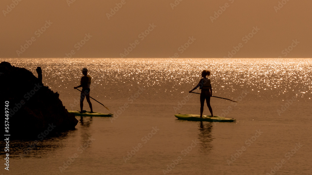 tourists relax on SUPs in the flat sea at sunset