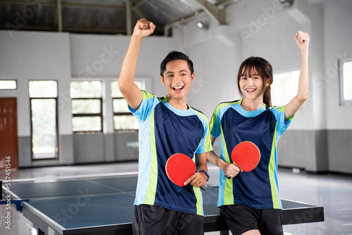 Two ping pong players holding paddles with raised fists near ping pong table photo