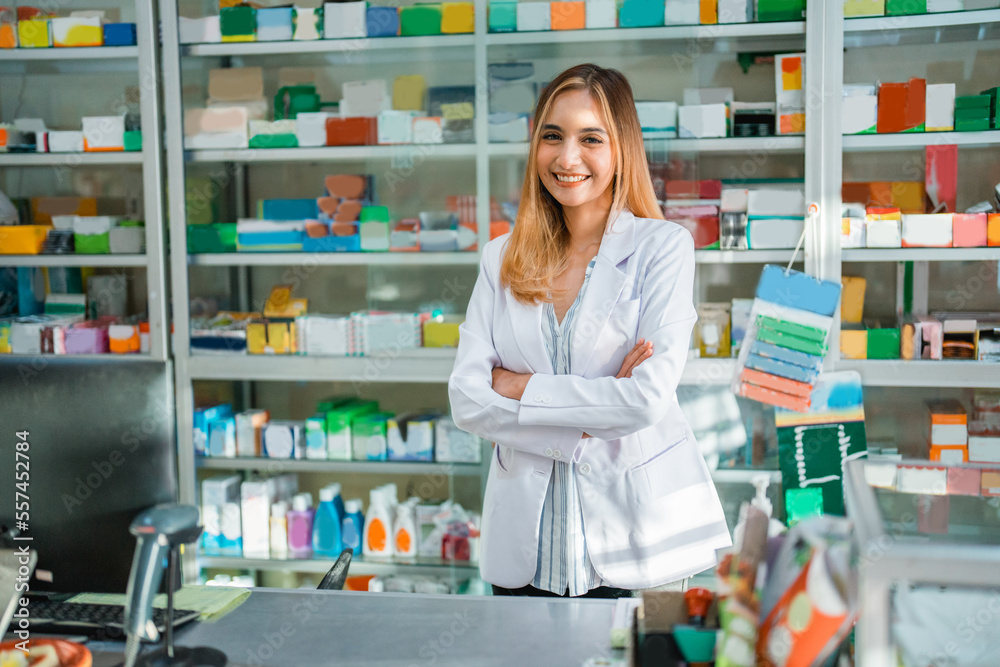 Attractive female pharmacist in uniform smiling at camera with crossed hands at pharmacy