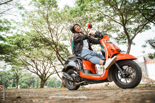Cheerful student girl wearing helmet and jacket riding motorbike to school