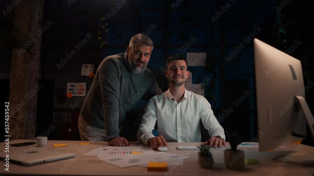 Male manager typing keyboard while working with experienced senior colleague in evening office Male manager typing keyboard while working with experienced senior colleague in evening office