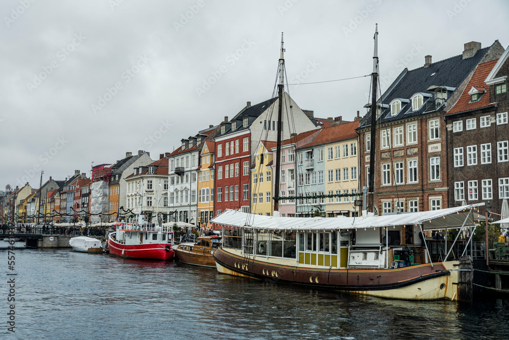 Nyhavn, a canal and entertainment district lined by brightly coloured 17th & 18th-century townhouses, with boats in the forground in Copenhagen during the day