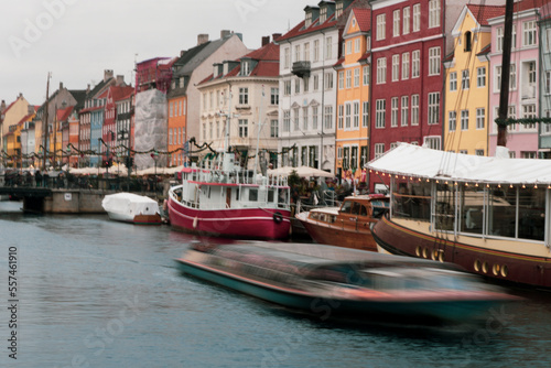 Long exposure of tour boat passing in front of Nyhavn a canal and entertainment district lined by brightly coloured 17th & 18th-century townhouses, in Copenhagen during the day