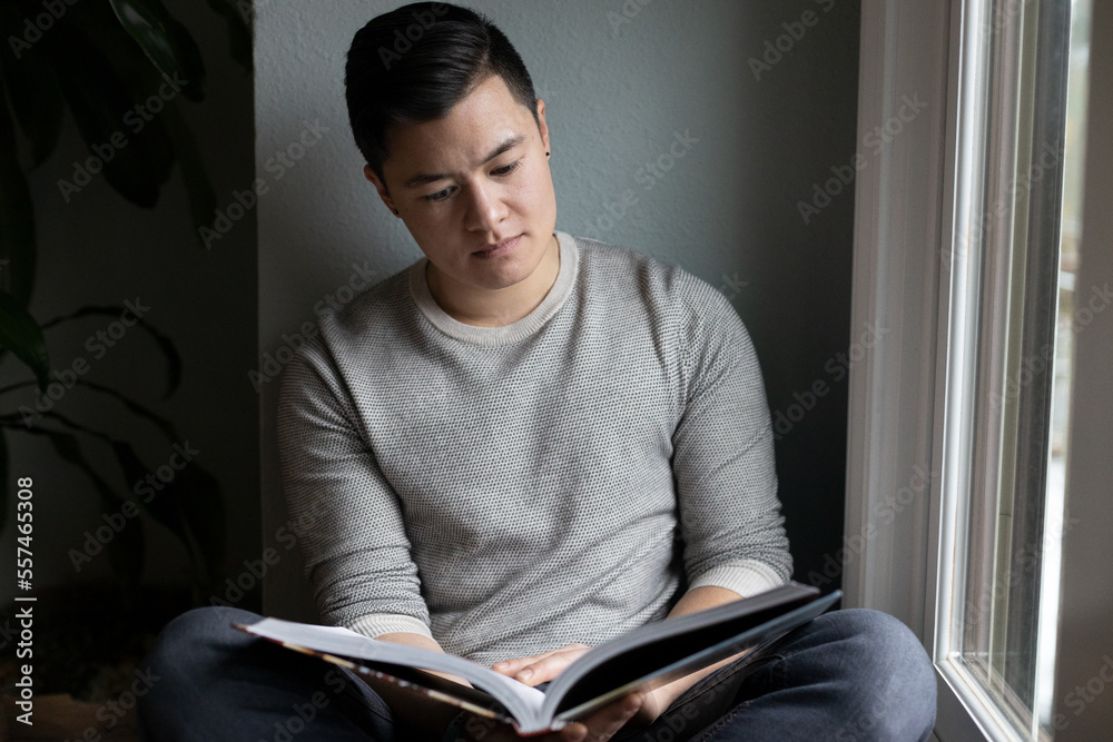 Fototapeta premium Asian American trans man sits by the windowsill.