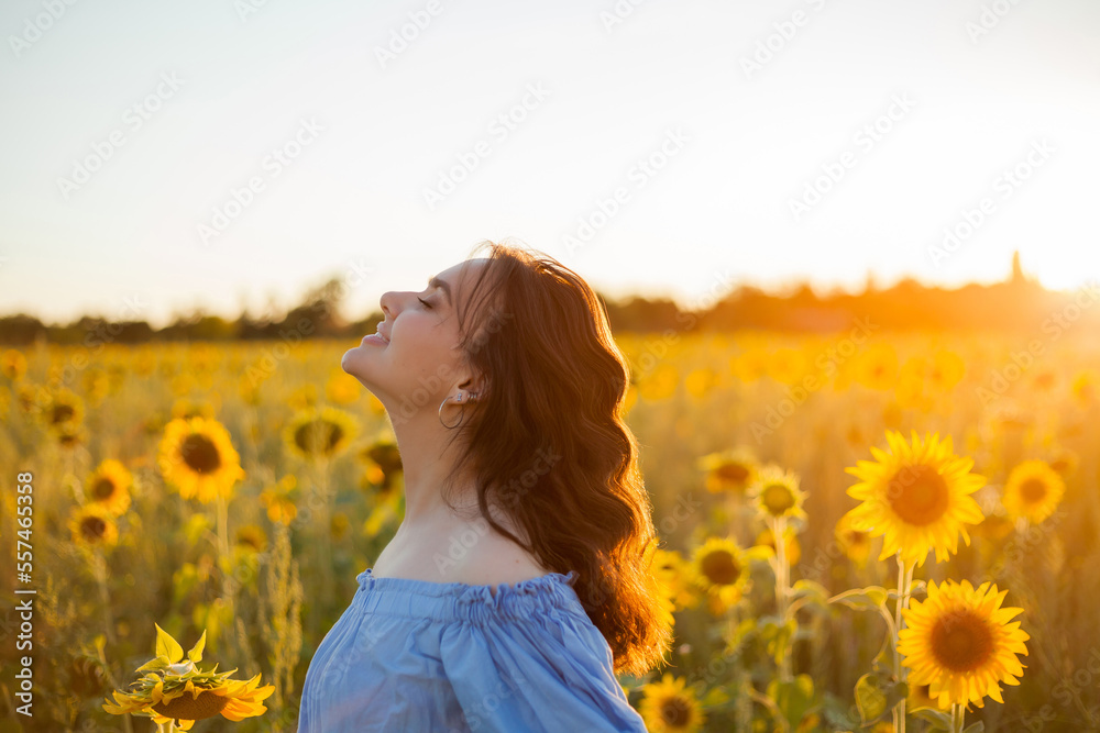 Beautiful young woman with dark curly hair in a sunflower field. Model in a stylish blue dress. Summer. Warmly.