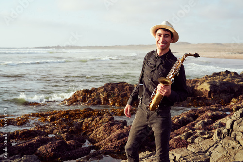 Canvas Print portrait young latino saxophonist standing on rocks smiling happy at sunset