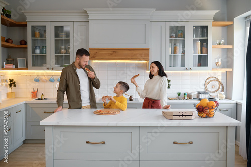 Parents and child eating pizza in living-room at home