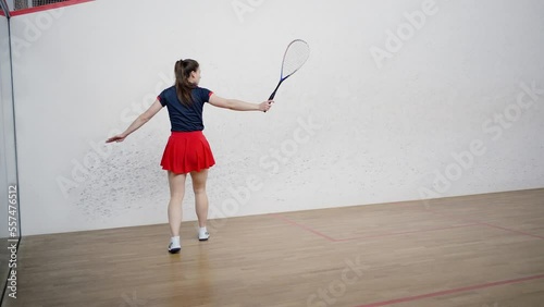 Brunette lady hits ball with racket standing on squash court photo