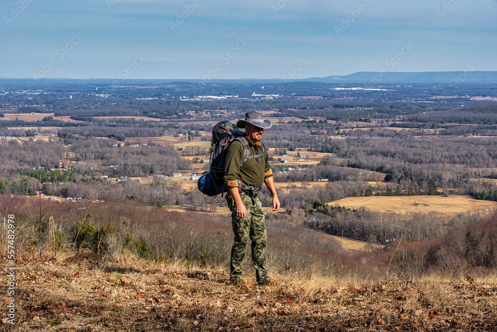 A man walking on a hiking trail with a backpack, camping on a mountain bluff overlooking the valley with Winchester Tennessee in the background.