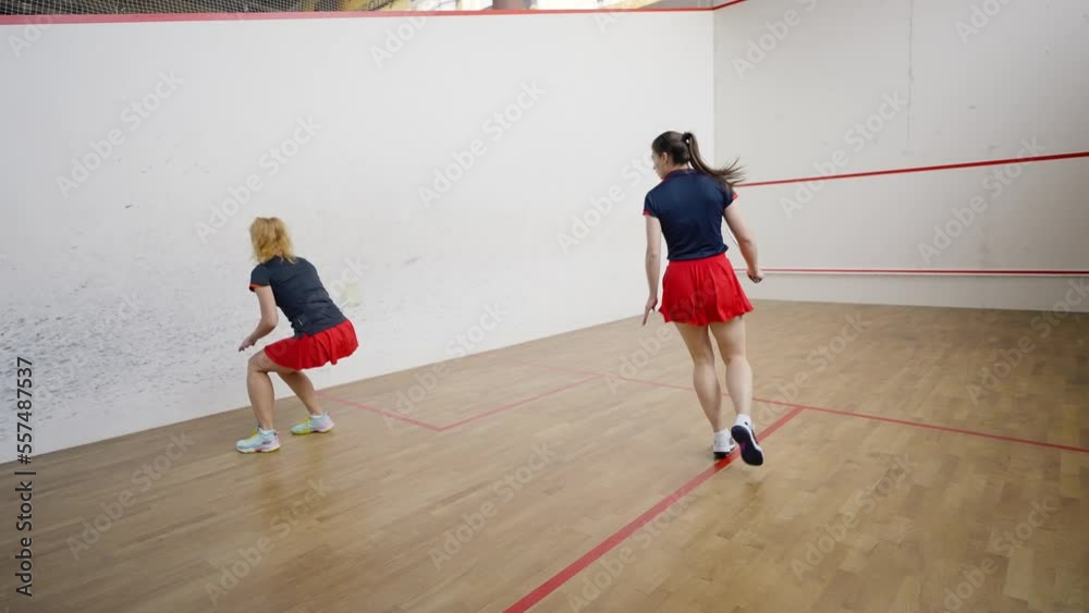 Sportive women take turns to hit ball against front wall Sportive women take turns to hit ball against front wall