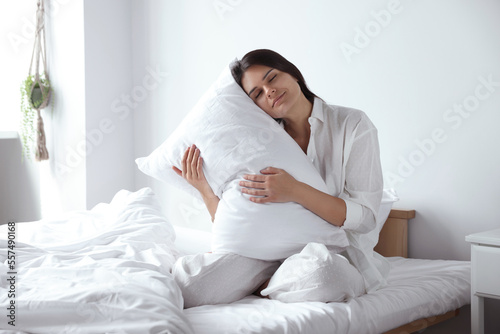 Beautiful young woman hugging pillow on bed at home